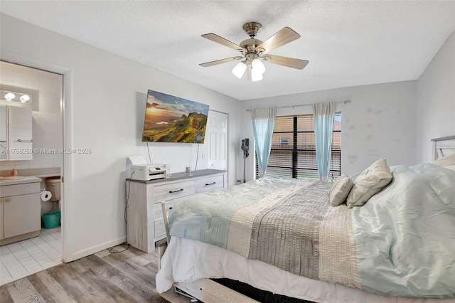 bedroom featuring light wood-style flooring, ensuite bathroom, ceiling fan, a textured ceiling, and baseboards