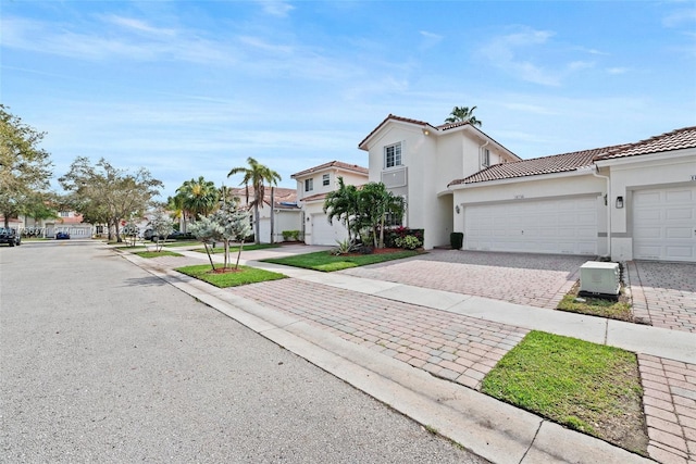 view of front of home with a tile roof, a garage, a residential view, decorative driveway, and stucco siding
