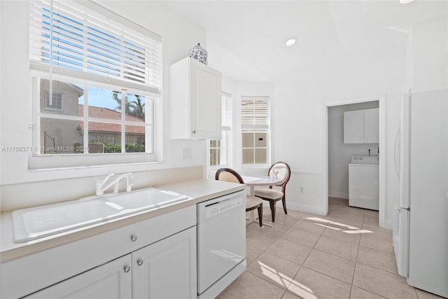 kitchen with white appliances, light tile patterned floors, washer / dryer, a sink, and white cabinetry