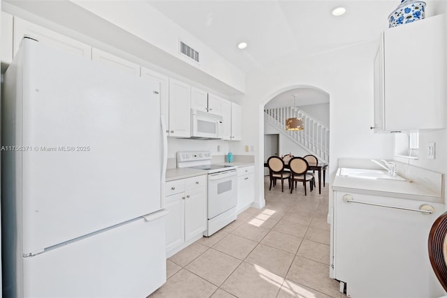 kitchen featuring light tile patterned floors, white cabinets, a sink, visible vents, and white appliances