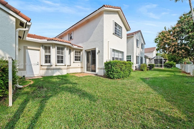 back of house featuring a tile roof, a lawn, and stucco siding