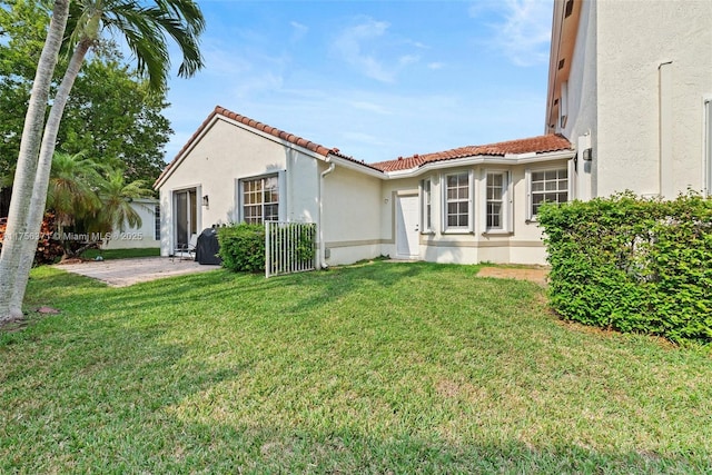 view of front of home with a front lawn, a patio, stucco siding, and a tiled roof