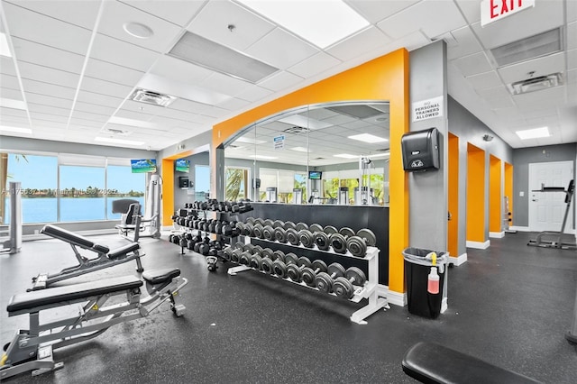 exercise room with a paneled ceiling, visible vents, and baseboards