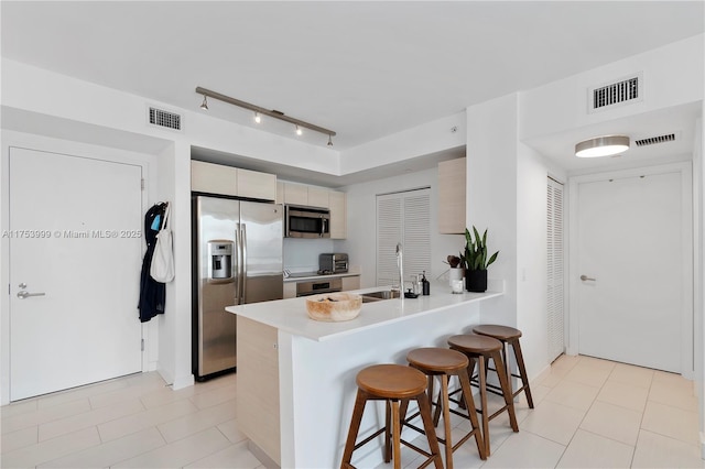 kitchen with a peninsula, appliances with stainless steel finishes, a kitchen bar, and visible vents