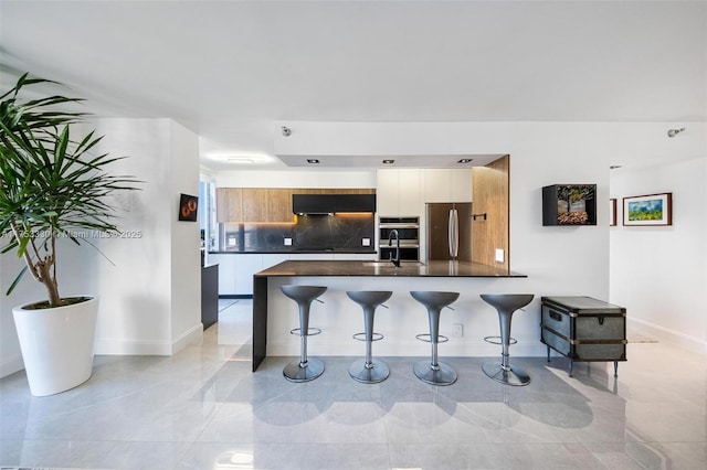 kitchen featuring stainless steel appliances, dark countertops, modern cabinets, a peninsula, and a kitchen bar