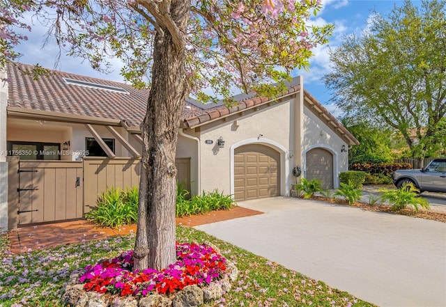 view of front of house featuring fence, concrete driveway, a tile roof, stucco siding, and a garage