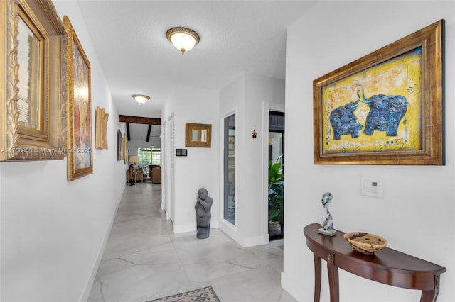 hall featuring a textured ceiling and baseboards