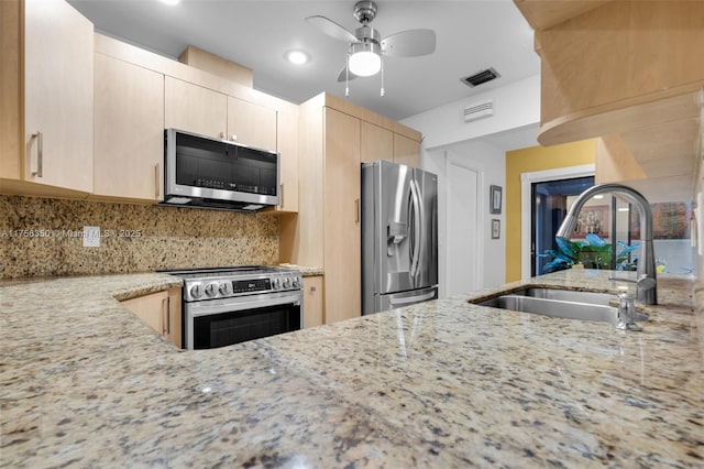 kitchen with light stone countertops, light brown cabinets, appliances with stainless steel finishes, and a sink