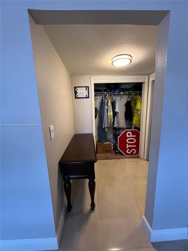 hall with baseboards, a textured ceiling, and tile patterned floors