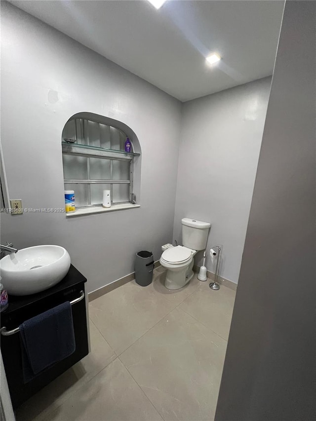 half bath featuring tile patterned flooring, baseboards, vanity, and toilet