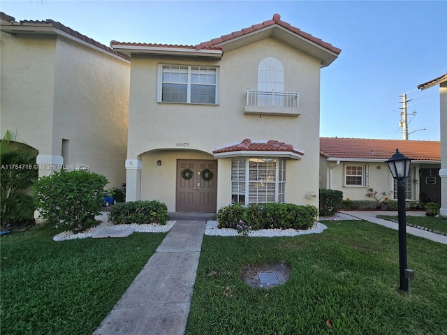 view of front of property featuring a tiled roof, a front lawn, a balcony, and stucco siding