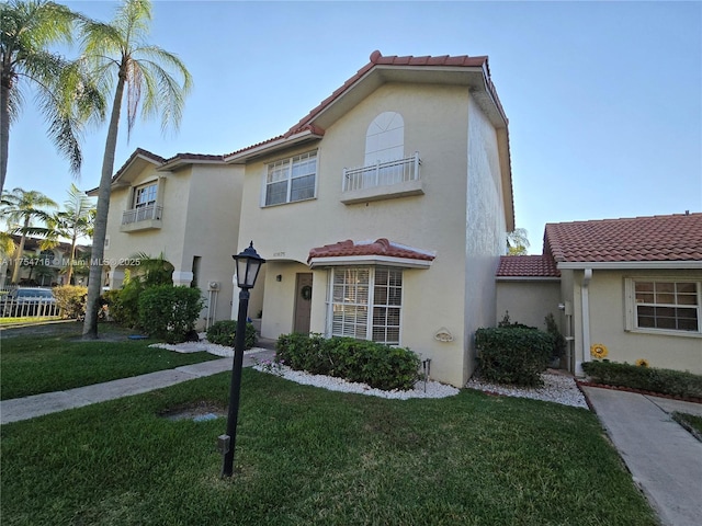 mediterranean / spanish house featuring a front yard, a tile roof, a balcony, and stucco siding