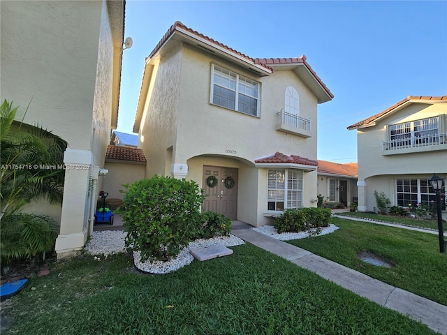 mediterranean / spanish house featuring a front yard, a tiled roof, and stucco siding