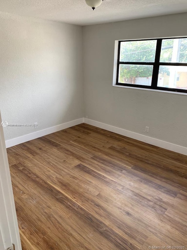 empty room featuring a textured ceiling, baseboards, wood finished floors, and a healthy amount of sunlight