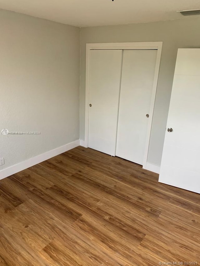 unfurnished bedroom featuring a closet, visible vents, baseboards, and wood finished floors