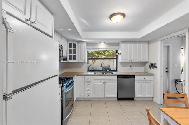 kitchen featuring light tile patterned floors, white cabinets, appliances with stainless steel finishes, a tray ceiling, and a sink