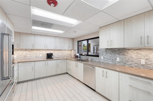 kitchen with appliances with stainless steel finishes, backsplash, a sink, and a paneled ceiling