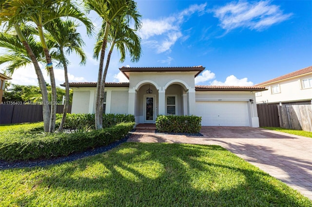 mediterranean / spanish home with an attached garage, fence, decorative driveway, stucco siding, and a front lawn