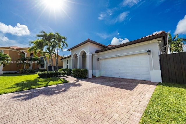 mediterranean / spanish house featuring a garage, a tile roof, decorative driveway, stucco siding, and a front lawn