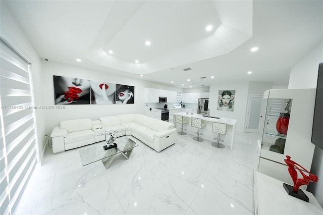 living room featuring marble finish floor, a raised ceiling, and recessed lighting