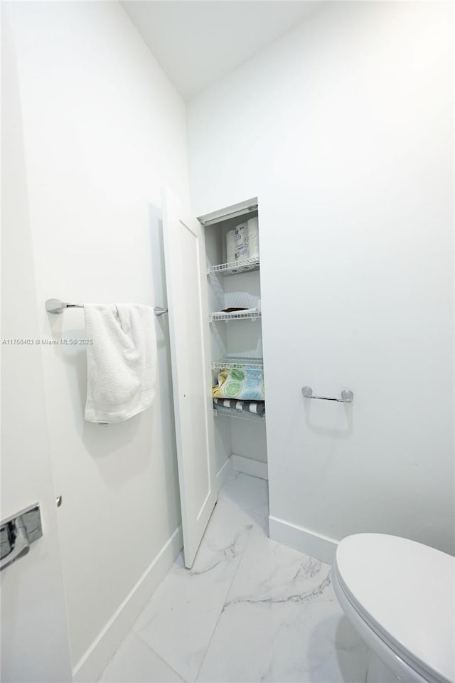 bathroom with toilet, marble finish floor, and baseboards