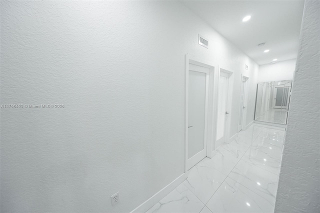 hall featuring a textured wall, recessed lighting, visible vents, baseboards, and marble finish floor