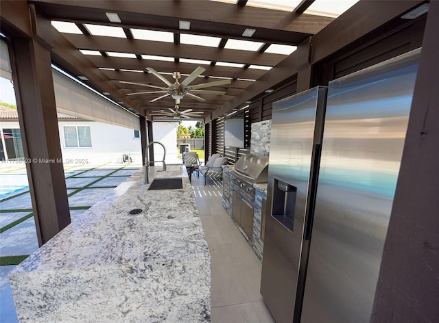 kitchen featuring light stone counters, a sink, a ceiling fan, modern cabinets, and stainless steel fridge