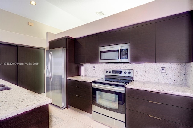 kitchen featuring light tile patterned floors, dark brown cabinetry, stainless steel appliances, decorative backsplash, and light stone countertops