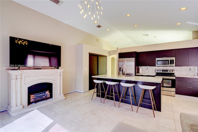 kitchen featuring a breakfast bar area, stainless steel appliances, lofted ceiling, backsplash, and a kitchen island with sink