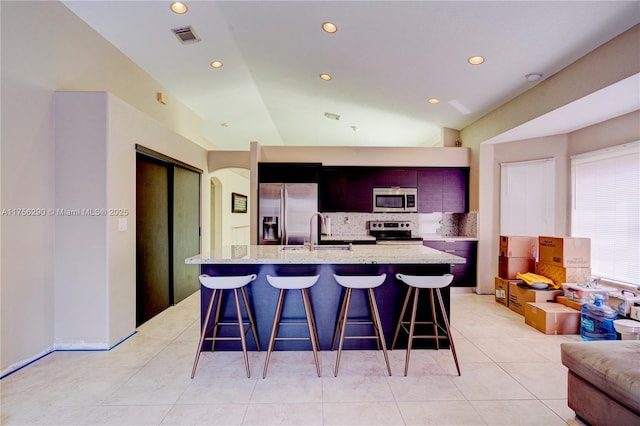 kitchen with arched walkways, stainless steel appliances, a sink, backsplash, and a kitchen bar