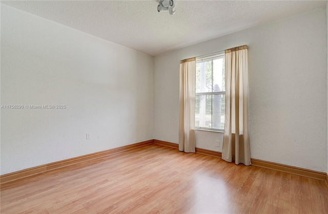 spare room featuring a textured ceiling, light wood-type flooring, and baseboards