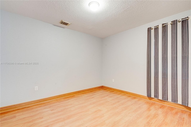 unfurnished room featuring visible vents, a textured ceiling, baseboards, and wood finished floors