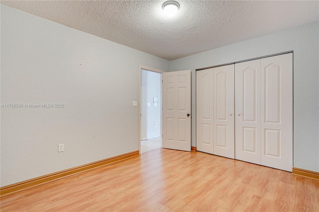 unfurnished bedroom with baseboards, a textured wall, wood finished floors, a textured ceiling, and a closet