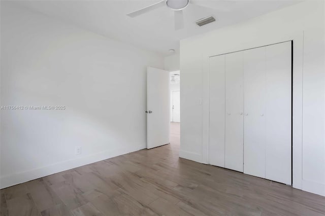 unfurnished bedroom featuring baseboards, visible vents, ceiling fan, wood finished floors, and a closet