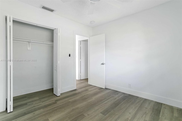 unfurnished bedroom featuring visible vents, a closet, baseboards, and wood finished floors