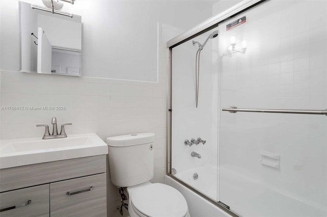 bathroom with vanity, tile walls, toilet, and bath / shower combo with glass door