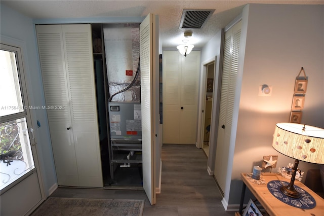 hallway with visible vents, a textured ceiling, baseboards, and wood finished floors