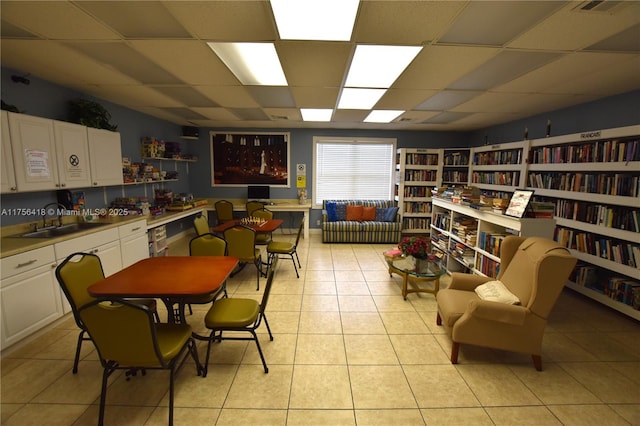 interior space with light tile patterned floors, bookshelves, and a drop ceiling