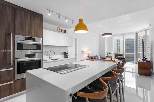 kitchen featuring a sink, expansive windows, black electric cooktop, stainless steel double oven, and backsplash