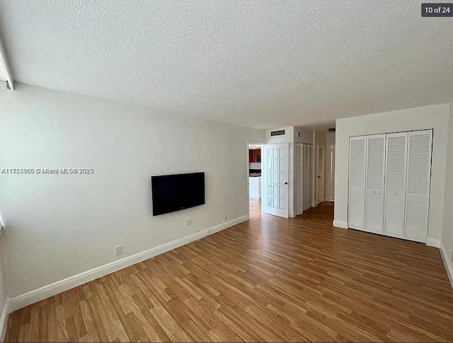 interior space featuring a textured ceiling, wood finished floors, visible vents, and baseboards