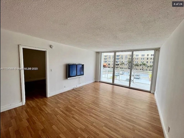 unfurnished living room with a wall of windows, a textured ceiling, baseboards, and wood finished floors