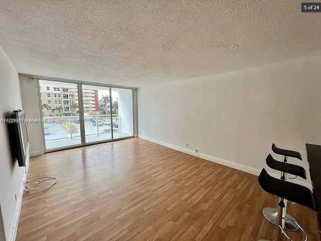 unfurnished room featuring baseboards, a textured ceiling, floor to ceiling windows, and wood finished floors