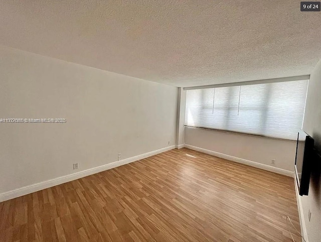 empty room with a textured ceiling, baseboards, and wood finished floors