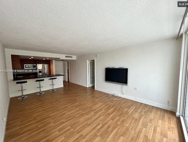 unfurnished living room featuring a textured ceiling, light wood finished floors, visible vents, and baseboards