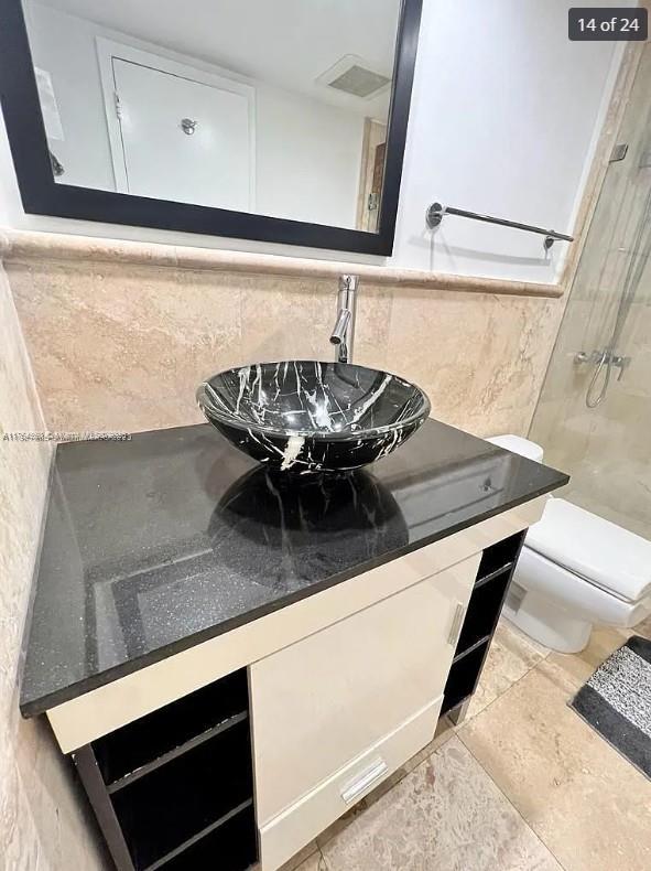 interior space with visible vents, toilet, vanity, a walk in shower, and tile walls