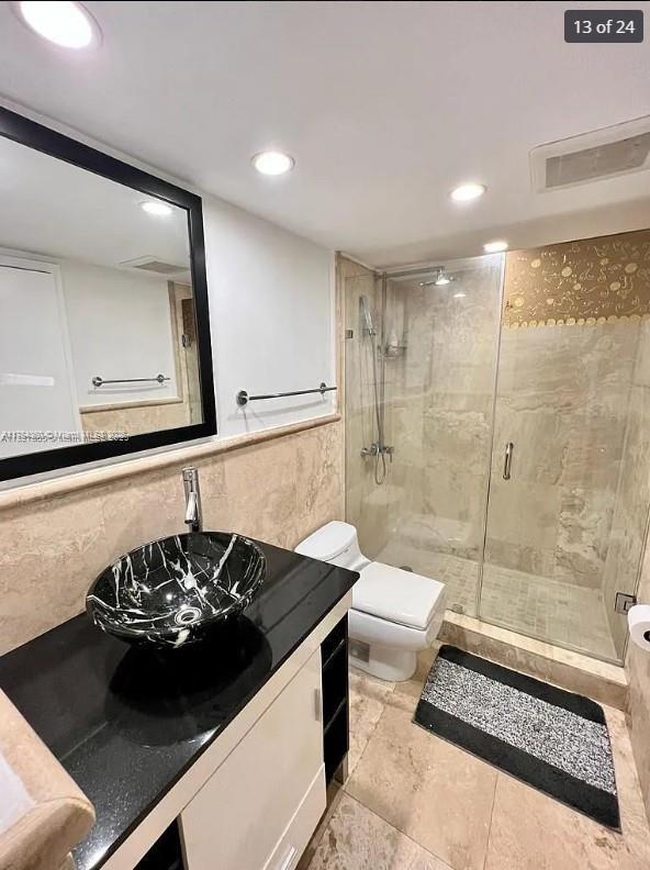 bathroom featuring tile walls, visible vents, toilet, a stall shower, and vanity