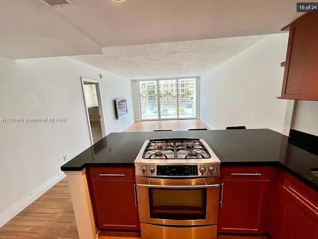 kitchen with dark countertops, light wood-style flooring, a peninsula, stainless steel gas range, and a textured ceiling