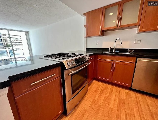 kitchen featuring a textured ceiling, light wood-style flooring, stainless steel appliances, a sink, and glass insert cabinets