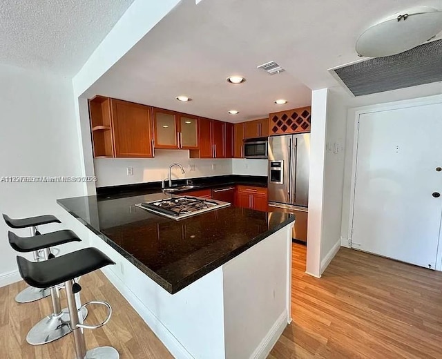 kitchen featuring visible vents, a peninsula, stainless steel appliances, light wood-type flooring, and a sink