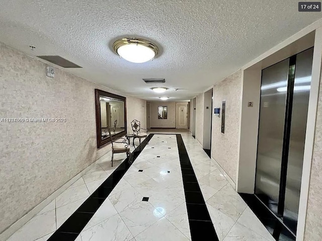 hallway with a textured ceiling, marble finish floor, and elevator